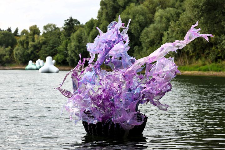 Aljoscha: Premeditatio Malorum auf dem Suitbertus-See Violette transparente Skulptur von Aljoscha auf dem Suitbertus-See in Düsseldorf-Kaiserswerth; im Hintergrund schwimmen weiße Körper der Installation BYCATCH vor dem bewaldeten Ufer