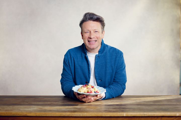 Jamie Oliver bei der Rolling Pin Convention 2026 Jamie Oliver sitzt in blauer Jacke an einem Holztisch und hält einen Teller in den Händen.