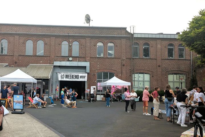 Hof Elegant Elephant Studios Hof der Elegant Elephant Studios in Düsseldorf-Lierenfeld beim Loft of Art Weekend Vol. 5, Besucher und Stände unter einem Banner mit der Aufschrift Loft of Art Weekend.