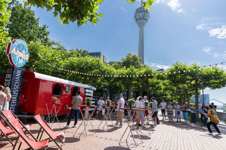 Apollo Rhein Rondell am Düsseldorfer Rheinufer Sonnenterrasse des Apollo Rhein Rondells in Düsseldorf mit rotem Ausschankwagen, Gästen und Blick auf den Rheinturm