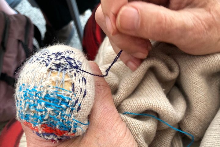 Kleidung reparieren mit Tina Miyake in Düsseldorf Hände reparieren einen hellen Strickpullover mit blauem Garn und einem Stopfei